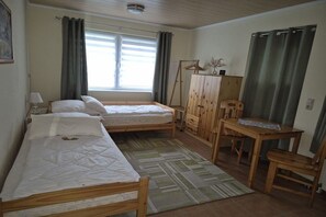 Ein Zimmer mit zwei Holzbetten, einem Schreibtisch aus Holz, einem Stuhl, einem Kleiderschrank und einem Fenster mit Vorhängen.
