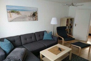 A living room with a sofa, a chair, a small table, a lamp, and a bookshelf. - Holiday home with 1 bedroom (Ostseebad Rerik)