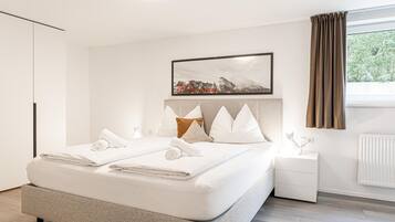 Une chambre moderne avec un grand lit, une table de chevet, une commode, un tableau encadré et une fenêtre avec des rideaux.