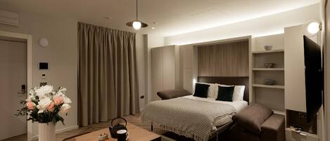 Ein modernes Hotelzimmer mit einem Bett, Nachttischen, einem Schreibtisch mit Stuhl, einer Blumenvase und einem Fernseher.