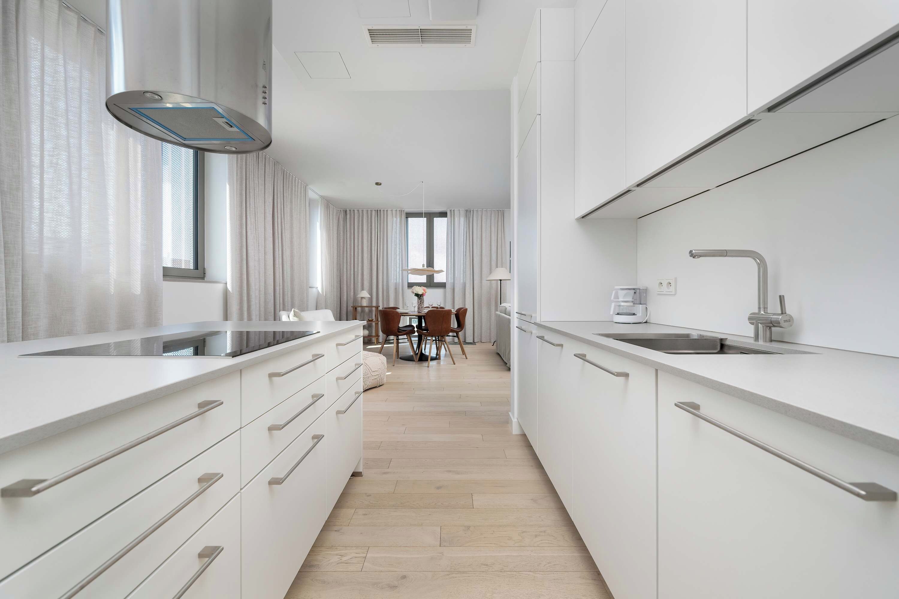 Una cucina moderna con mobili bianchi, forno integrato e lavello in acciaio inossidabile.
