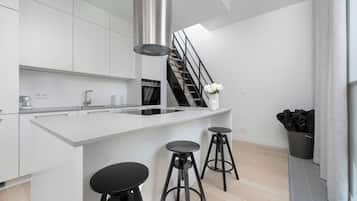 Eine moderne Küche mit einer zentralen Kochinsel, schwarzen Barhocker und einer Treppe, die in eine obere Etage führt.