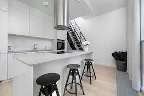 Eine moderne Küche mit einer zentralen Kochinsel, schwarzen Barhocker und einer Treppe, die in eine obere Etage führt.