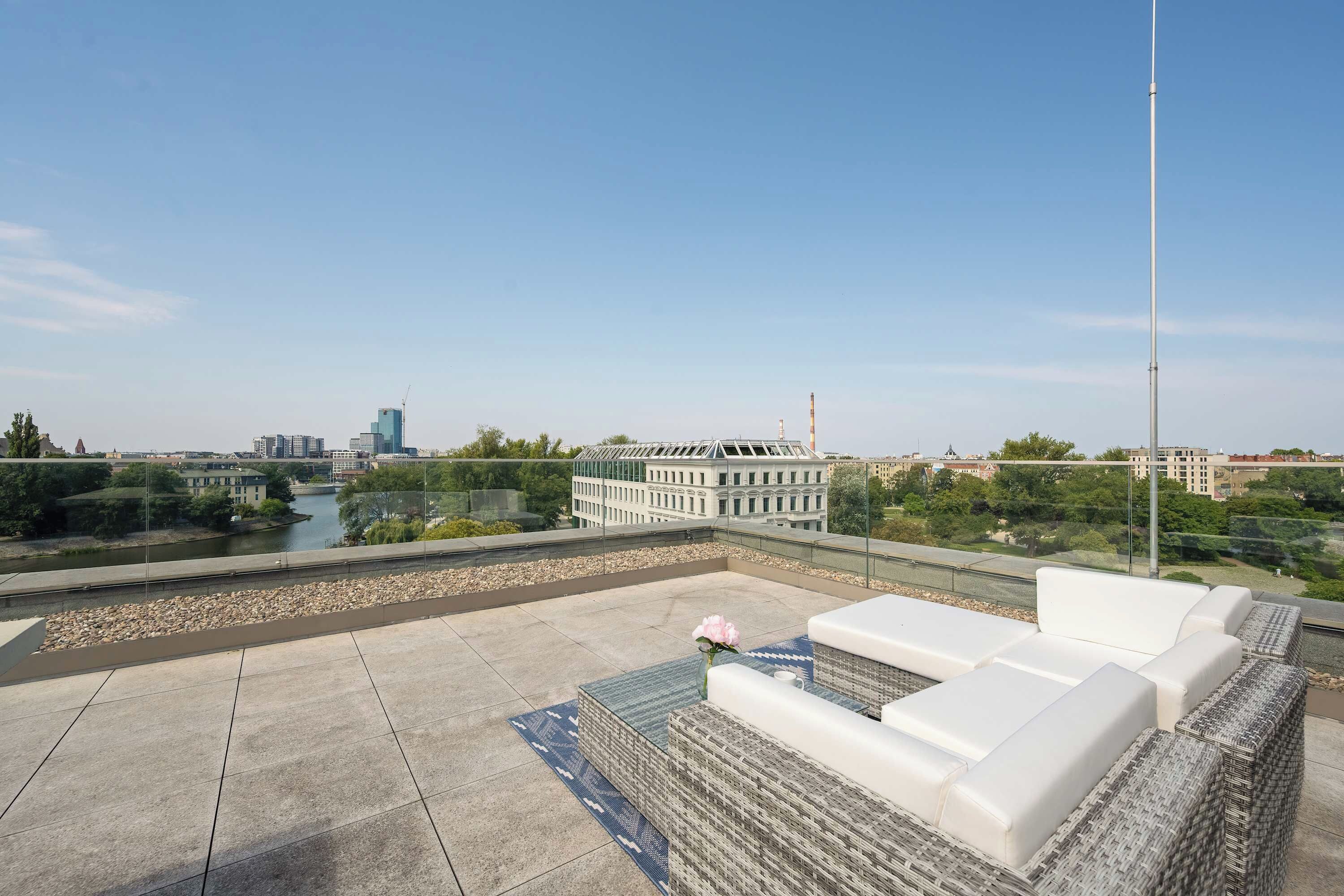 A rooftop terrace with a view of a river, buildings, and a clear sky.