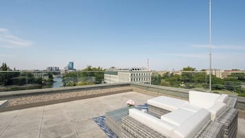 A rooftop terrace with a view of a river, buildings, and a clear sky.
