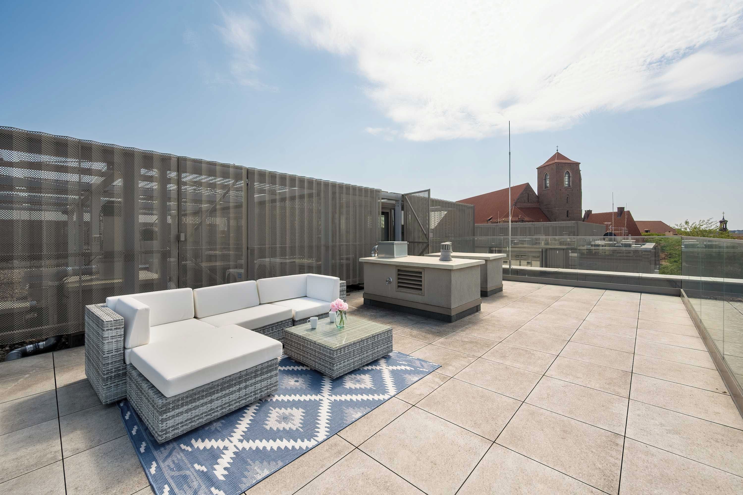 Eine Dachterrasse mit einer weißen Couch, einem kleinen Tisch und einem gemusterten Teppich.