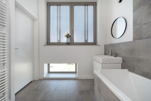 Ein modernes Badezimmer mit großem Fenster, Waschbecken in Weiß, Spiegel und Badewanne.