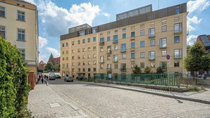 Um edifício de vários andares com fachada de tijolos, várias janelas e uma cerca de metal verde.