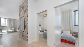 Quarto moderno com um espelho grande, cama com estrutura vermelha e vista para a paisagem urbana pela janela.