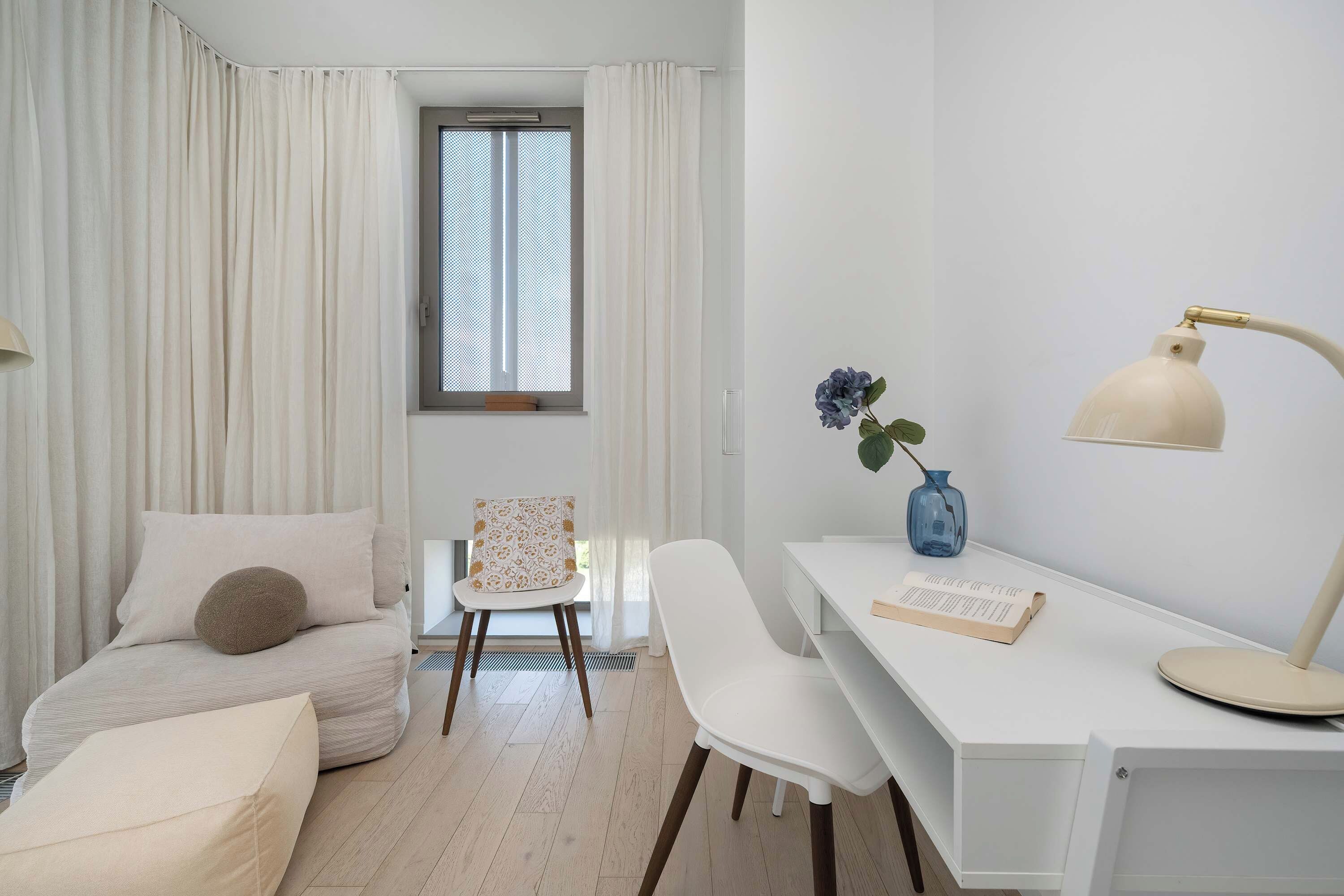 Ein schlicht eingerichtetes Zimmer mit Bett, Schreibtisch, Stuhl und einem blickdichten Fenster.