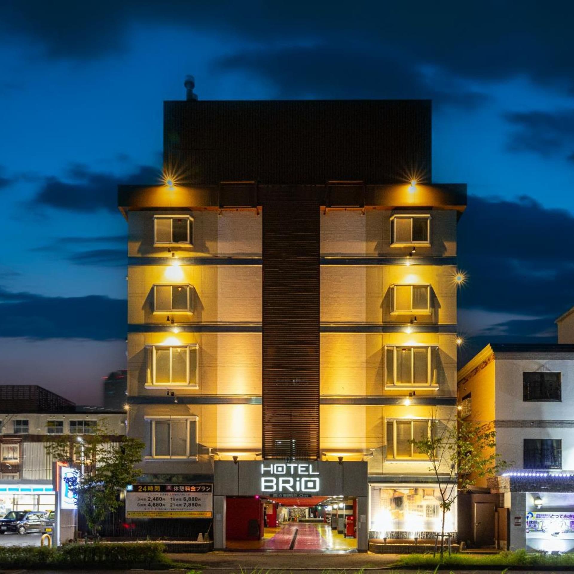 Ein mehrstöckiges Hotel mit zentralem Eingang, beleuchteten Fenstern und einer Schilder mit der Aufschrift 'HOTEL BRIO'.