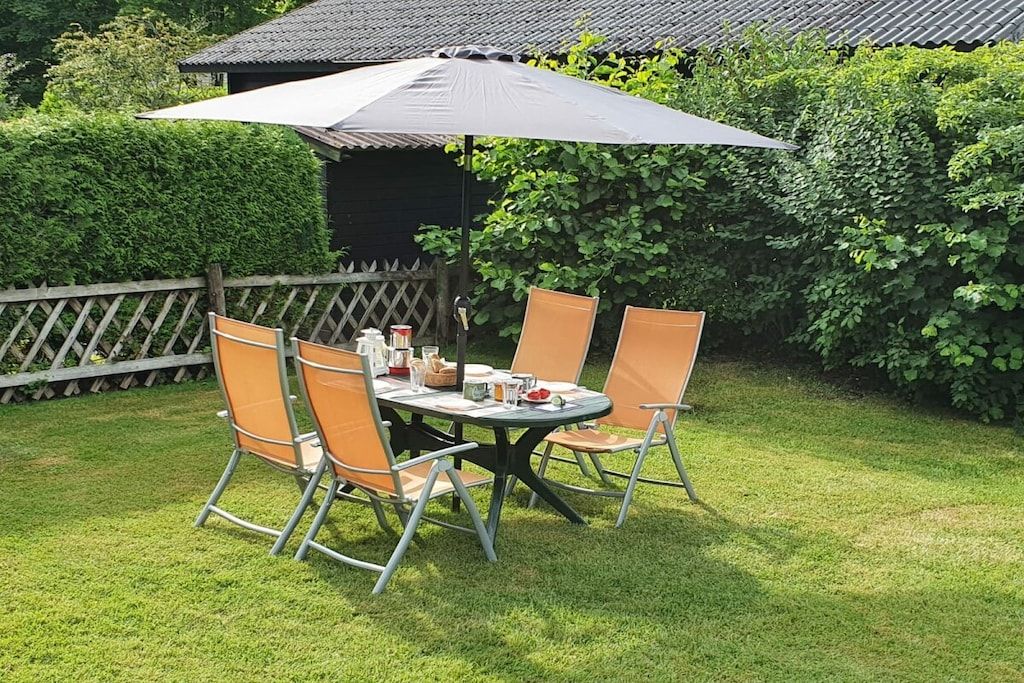 An outdoor dining area with a table and chairs, a large umbrella, and a wooden fence.