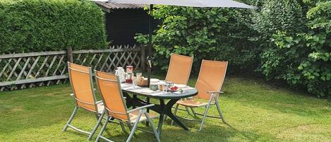 An outdoor dining area with a table and chairs, a large umbrella, and a wooden fence.