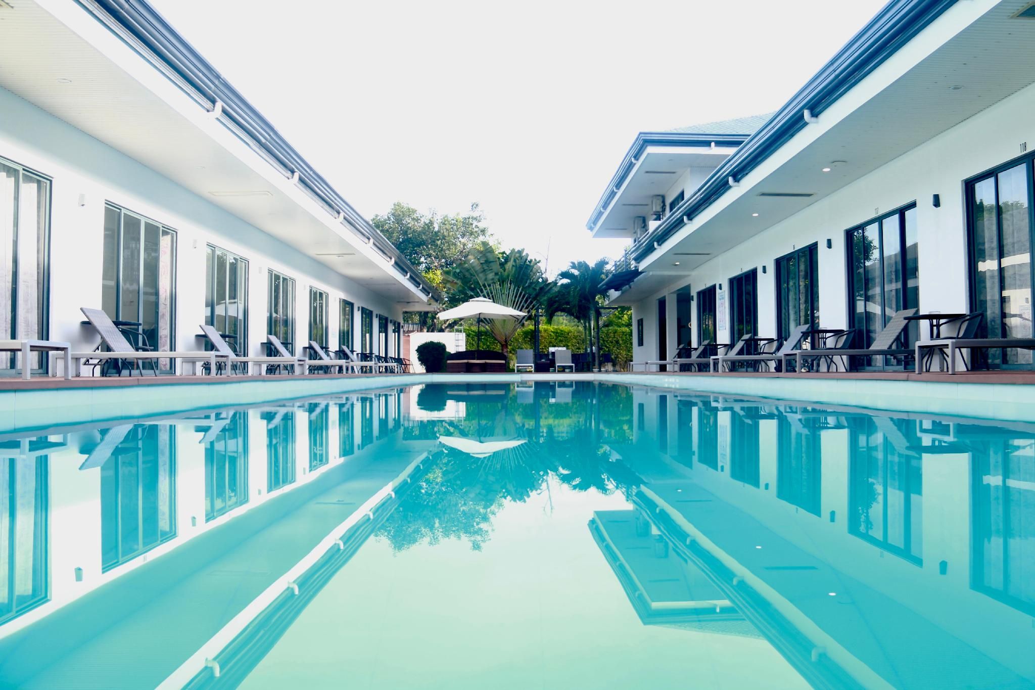 A swimming pool with lounge chairs and umbrellas, surrounded by modern buildings with large windows.