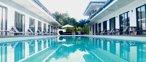 A swimming pool with lounge chairs and umbrellas, surrounded by modern buildings with large windows.