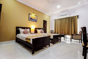Quarto de hotel com cama de casal, área de estar com uma poltrona, uma mesa pequena e um quadro na parede.