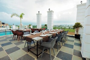 An outdoor dining area with tables and chairs, a pool, and a view of the cityscape. - Revaas Lake View Boutique Hotel (Udaipur)
