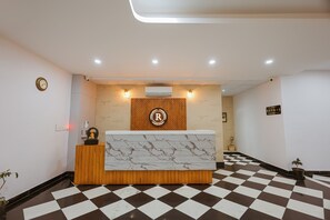 A reception desk with a marble top, a wooden panel wall with a logo, and a checkered floor. - Revaas Lake View Boutique Hotel (Udaipur)