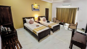 A hotel room with two beds, a desk, a chair, a coffee table, a wardrobe, and an air conditioning unit. - Revaas Lake View Boutique Hotel (Udaipur)