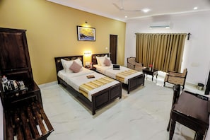 Quarto de hotel com duas camas, uma escrivaninha, uma cadeira, uma mesa de centro, um guarda-roupa e um ar condicionado.