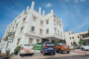 A multi-story building with a white facade and multiple chimneys. There are cars parked in front, and a gated entrance is visible. - Revaas Lake View Boutique Hotel (Udaipur)