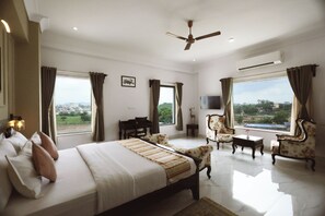 A hotel room with a bed, a desk, a chair, a television, and large windows. - Revaas Lake View Boutique Hotel (Udaipur)