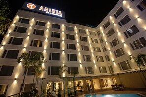 A multi-story hotel with a sign reading 'ARISTA' and a pool area with lounge chairs and umbrellas. - Arista By Ambition - Guwahati (Guwahati)