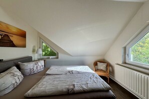 Een kamer met twee bedden, een raam, een stoel en een schilderij aan de muur.