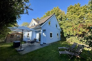 Ein zweistöckiges Haus mit Terrasse, kleiner Holzterrasse und Garten.