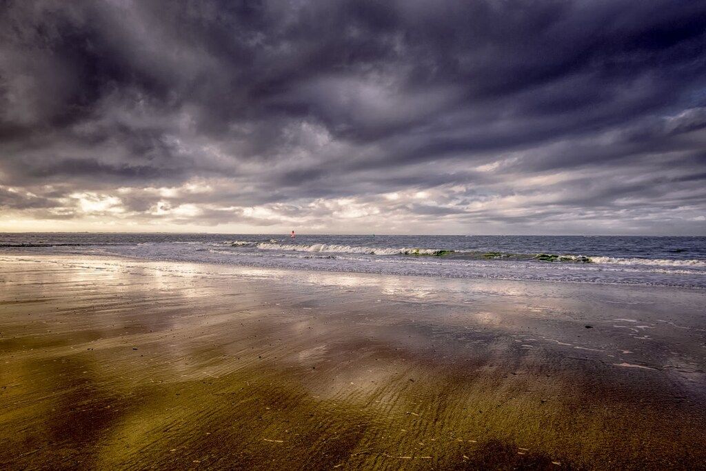 A beach with a wet sand surface and a cloudy sky.