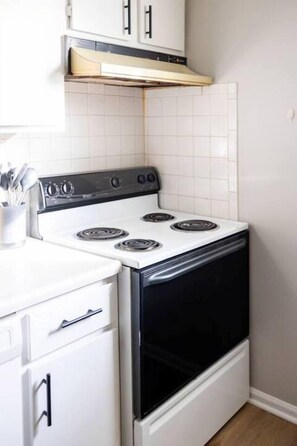 A kitchen with a white stove, black oven, and white cabinets. - The Fremont Flats | Near Downtown | with WiFi (Manhattan)