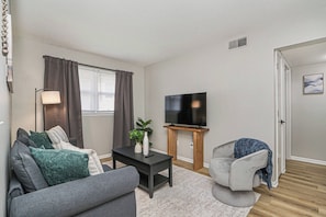 A living room with a sofa, a coffee table, a TV on a stand, a lamp, and a door. - The Fremont Flats | Near Downtown | with WiFi (Manhattan)