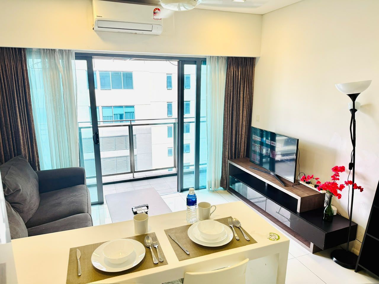Habitación de hotel con comedor, sofá, televisión y balcón con vistas a edificios.