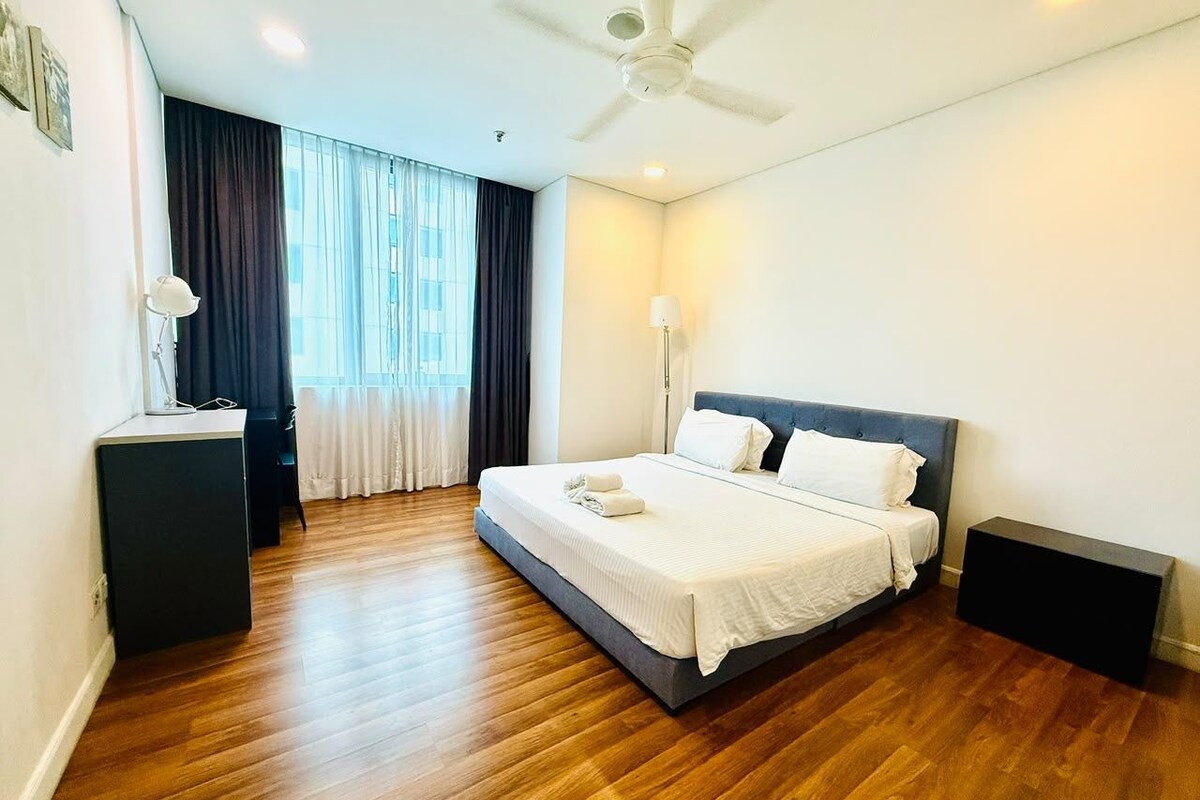 A hotel room with a bed, bedside tables, a desk, a ceiling fan, and a window with curtains.