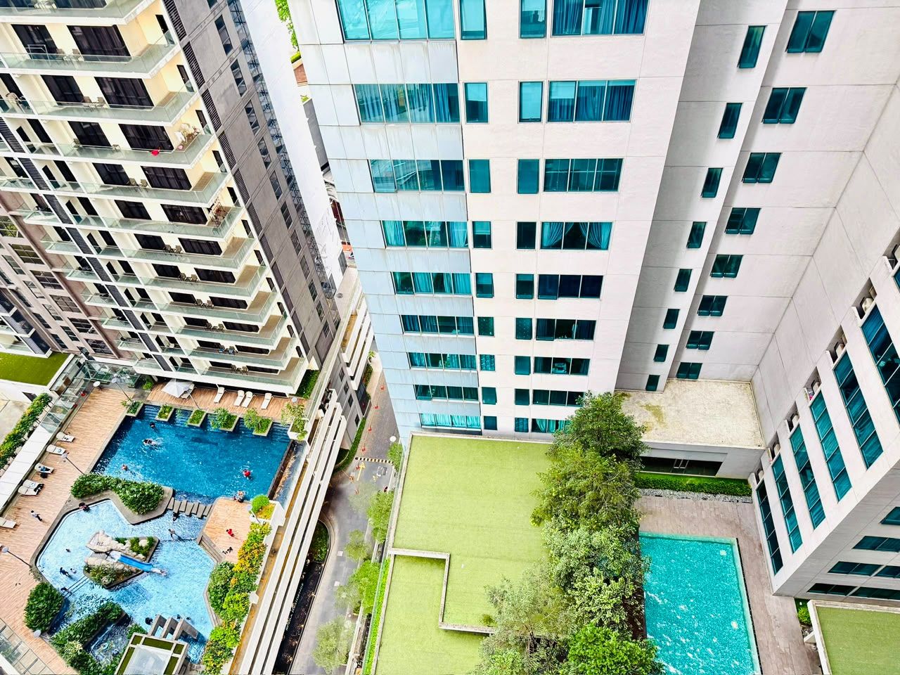 A high-rise building with multiple balconies, a rooftop pool, and a green lawn area.