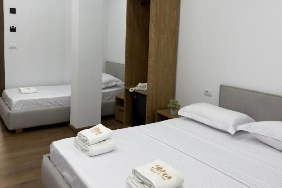 A hotel room with a large bed, a smaller bed, a wooden wardrobe, and a nightstand with a lamp.