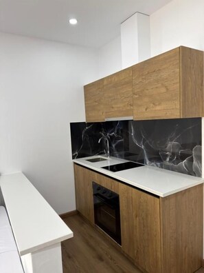 A modern kitchen with wooden cabinets, a black marble backsplash, and a built-in oven. - Petro Rooms and View (Vau-Dejës)