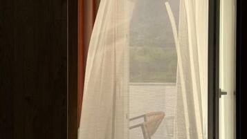 Una habitación con vistas al exterior, visible a través de una ventana con cortinas translúcidas, una puerta de madera y una silla.