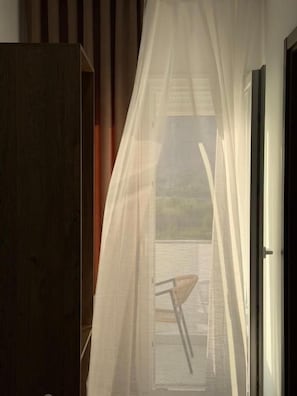 A room with a view through a window with sheer curtains, a wooden door, and a chair visible outside.
