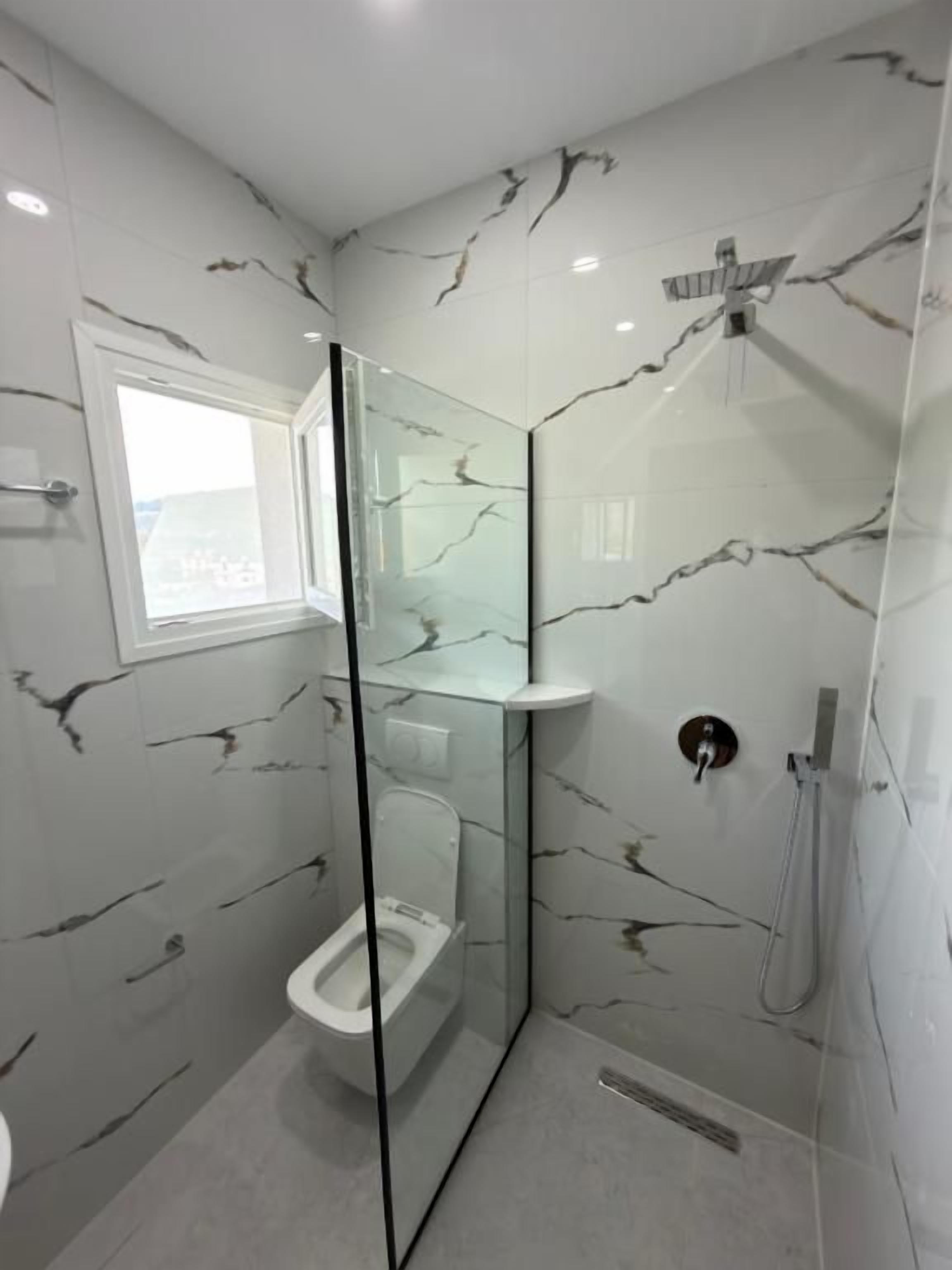 A modern bathroom with a glass-enclosed shower, a toilet, and a window.