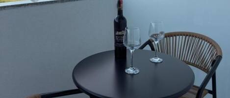 A balcony with a table, two chairs, a bottle of wine, and two glasses.