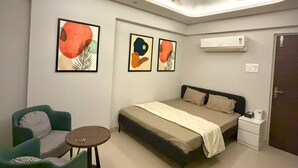 A modern bedroom with a bed, a chair, a small table, and abstract art on the walls. - Slate VII by Ved Homes (Jaipur)