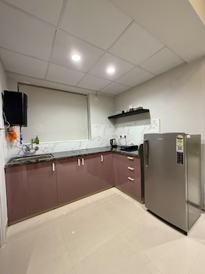 Eine Küche mit einem Edelstahl-Kühlschrank, Marmor-Spritzschutz und einem flachbildfernseher an der Wand.