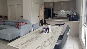 Een moderne woonruimte met een grijze hoekbank, een eettafel met stoelen, en een keuken met kasten en apparatuur.