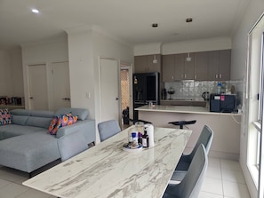 A modern living space with a grey sectional sofa, a dining table with chairs, and a kitchen area with cabinets and appliances. - Relaxing Gateway: Private Room 1 (North Lakes)