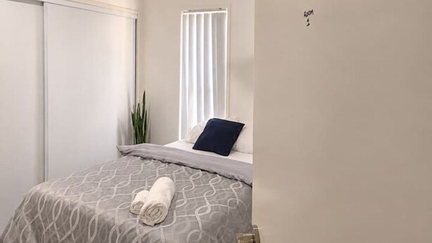 Een slaapkamer met een bed, een plafondventilator, een raam met zonwering en een plant.