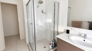 Een moderne badkamer met een douchecabine van glas, een witte wastafel en een grote spiegel.