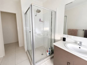 A modern bathroom with a glass shower enclosure, a white sink, and a large mirror. - Relaxing Gateway: Private Room 1 (North Lakes)