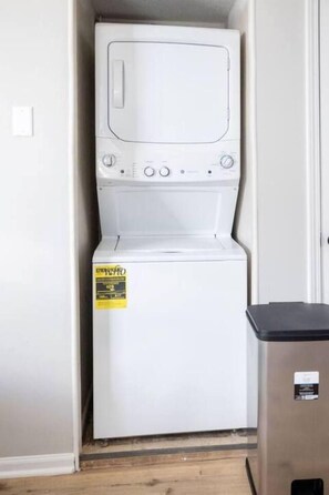 A compact, white, front-loading washing machine in a small laundry room with a wooden floor. - Fremont Stylish Stay | Near K-State | Free Parking (Manhattan)
