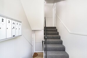 A staircase with carpeted steps and a metal handrail, leading to a landing with a door. - Fremont Stylish Stay | Near K-State | Free Parking (Manhattan)